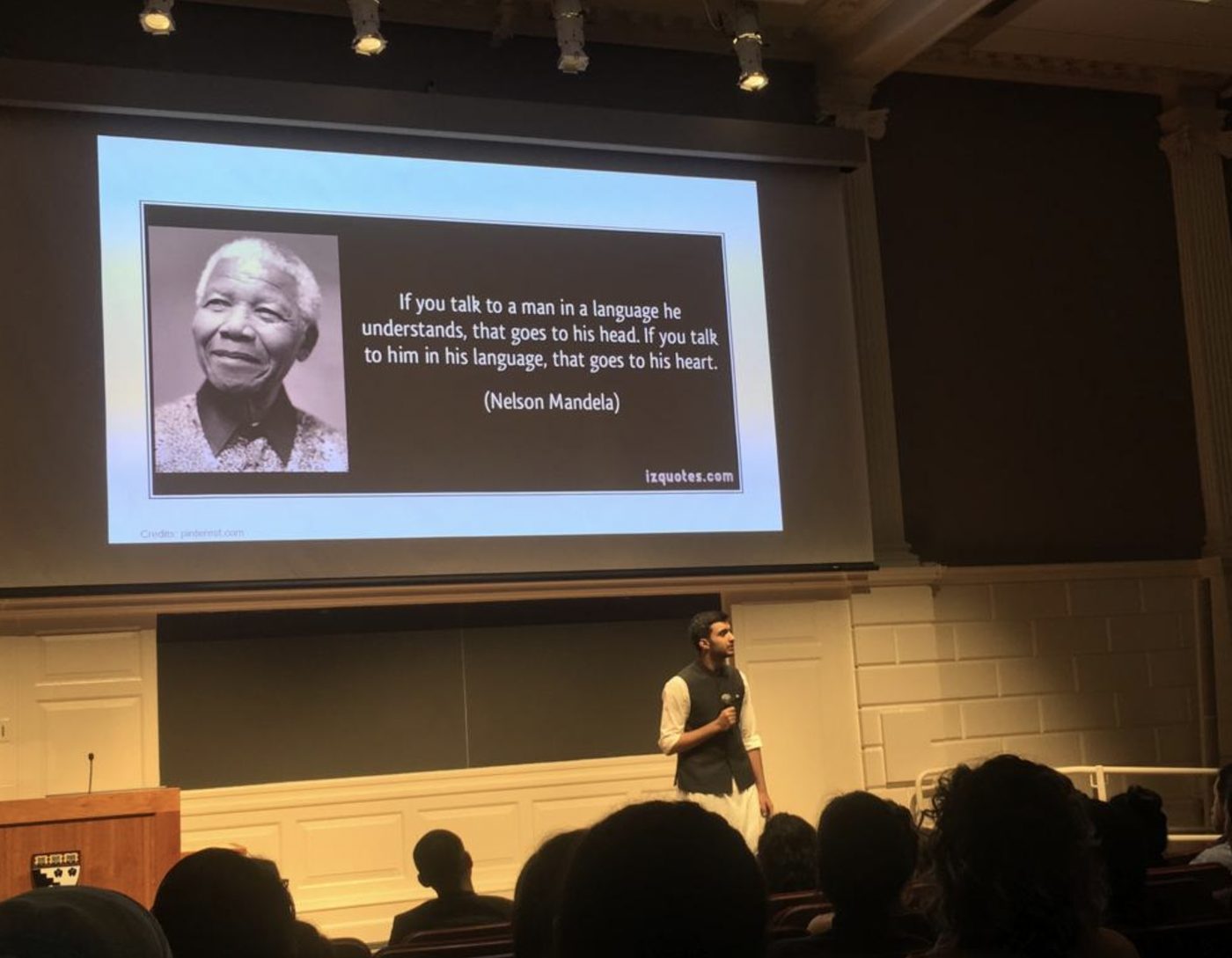 Umair on stage at the HGSE Ed Talks, beneath a slide of Nelson Mandela's quote about speaking to a man in his own language
