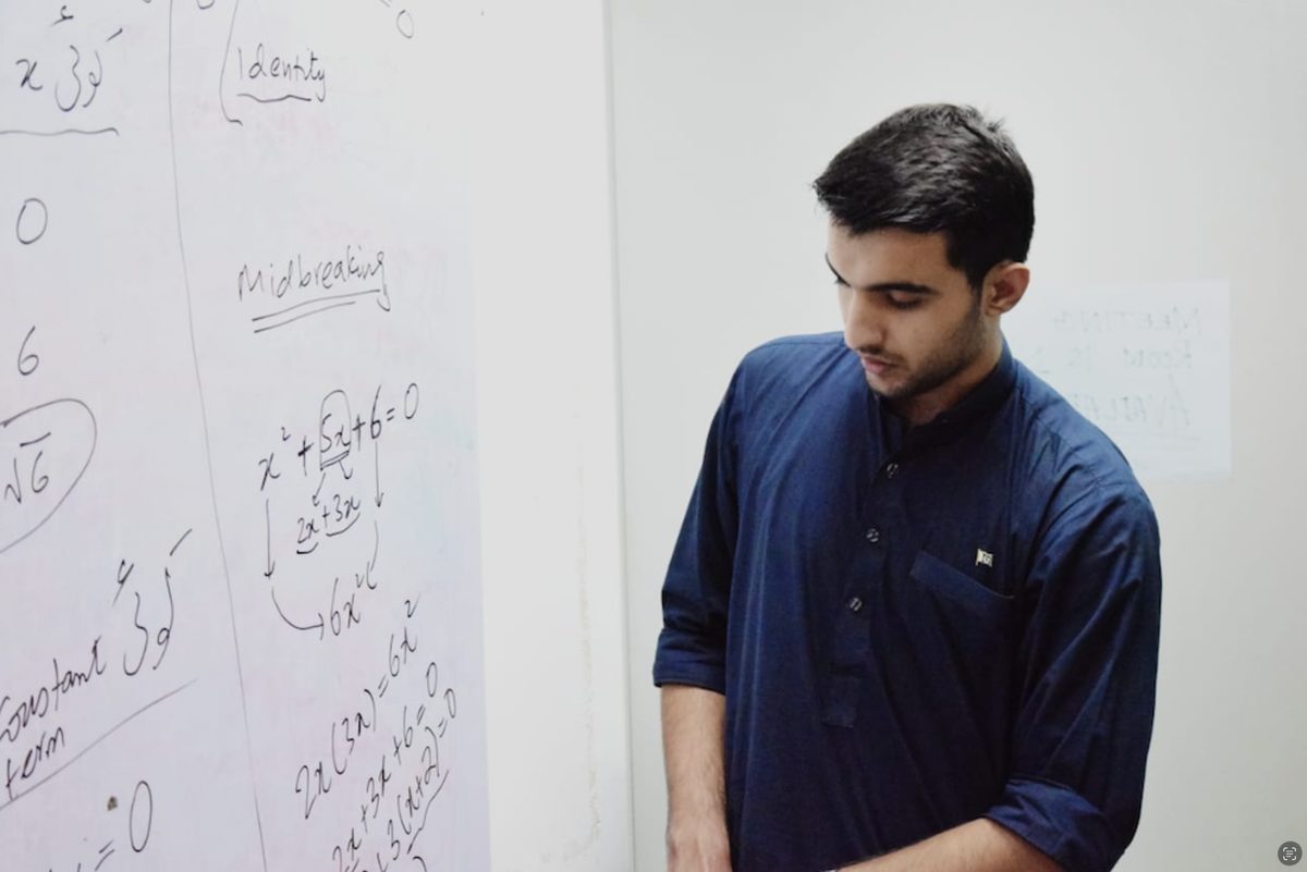 Umair working through quadratic factoring at a whiteboard